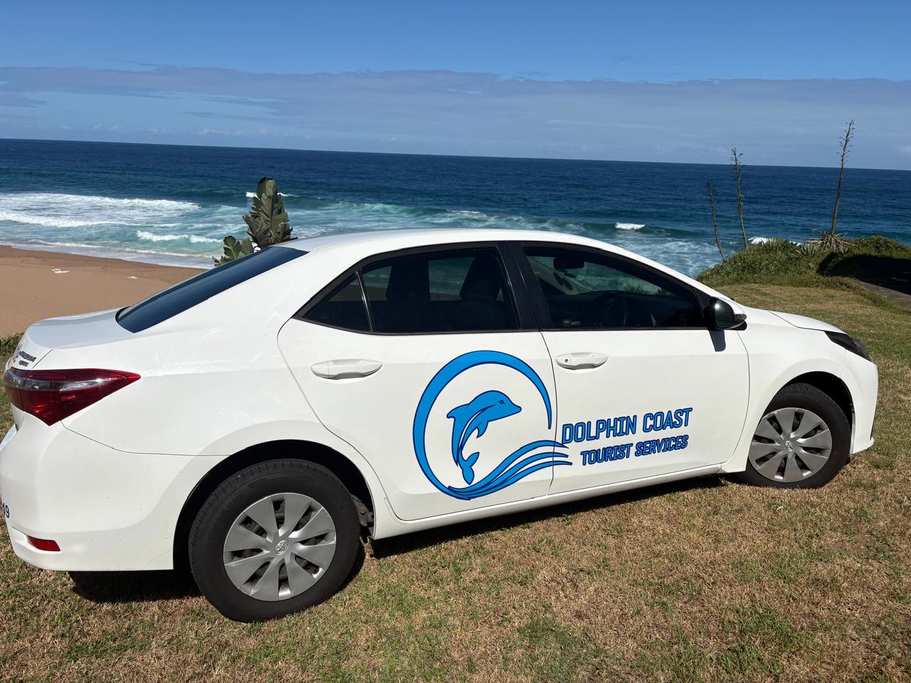 A branded Dolphin Coast Tourist Services sedan parked above the beach at Ballito