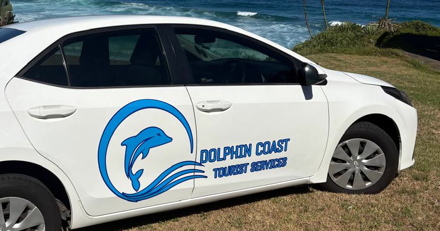 The Dolphin Coast Tourist Services sedan with the surf behind it